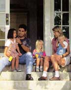 Family sitting on porch with front door of house open behind them